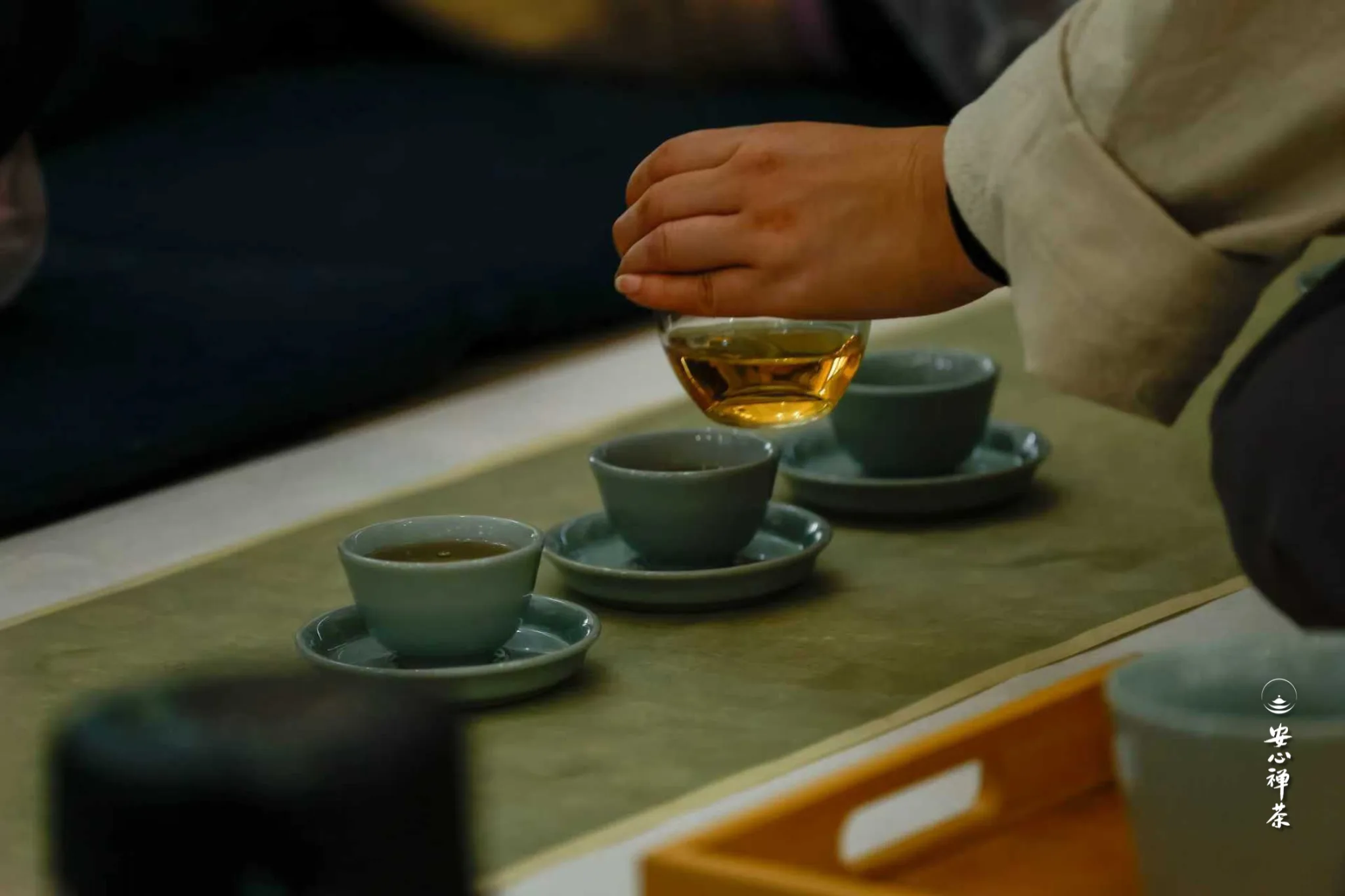 手持茶杯倒茶,木质茶盘上排列多个青瓷茶盏