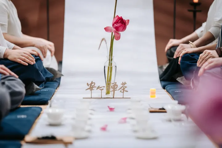 参加者围坐在桌前,中央放置一支粉红色莲花在玻璃瓶中,旁边有木制禅意装饰和蜡烛
