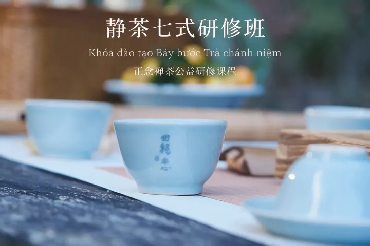 浅蓝色茶杯和茶叶放在木质茶盘上,背景有茶具和植物